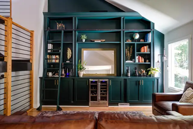 Dark green built-in bookcases with a rolling library ladder, a wine fridge and a leather sofa in a lounge room