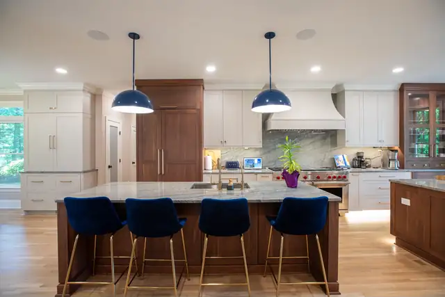 Large kitchen with a dark wood island, navy velvet stools, navy dome pendants and a white range hood over a stone backsplash