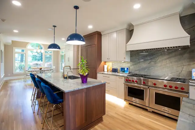 Kitchen with a dark wood island, blue velvet counter stools, a white range hood over a stone slab backsplash and a professional range