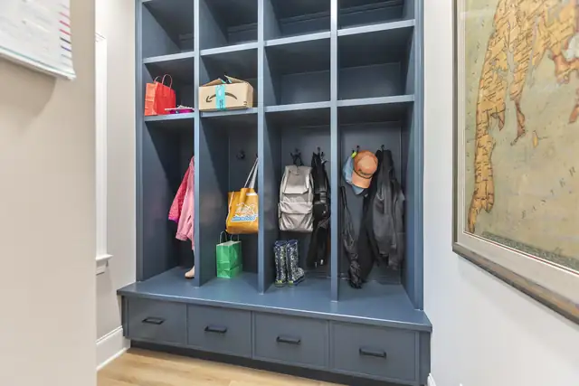 Blue-gray built-in mudroom lockers with hooks, open cubbies and drawers below