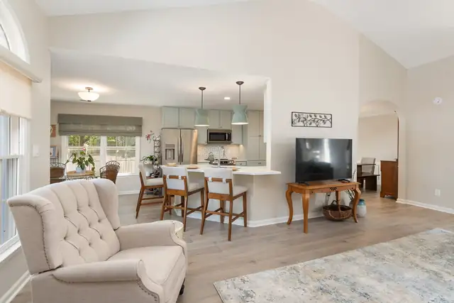 Open family room with wood-look floors that flows into a remodeled kitchen with a sage island and counter seating