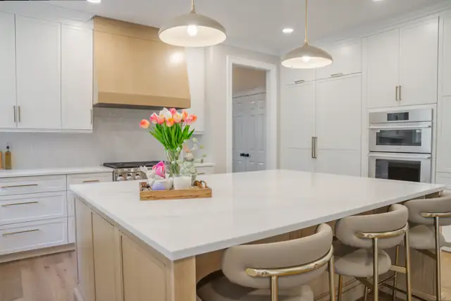 Cary kitchen with white cabinets, a natural wood range hood, a light wood island with a white top and brass pendant lights