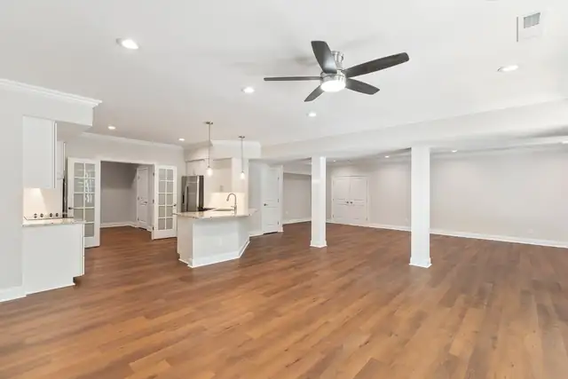 Large finished lower level with wood-look floors, white columns, a ceiling fan and a kitchenette