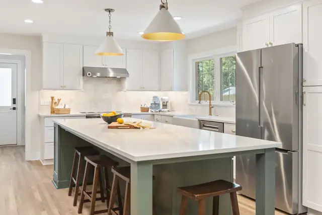 Kitchen with white cabinets, a sage green island with a white top, wood counter stools and cone pendant lights
