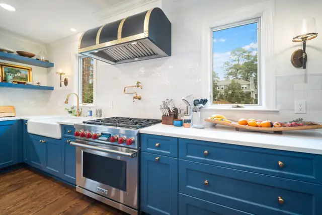 Durham kitchen in Hope Valley with blue cabinets, a farmhouse sink, a pot filler and a black and brass range hood